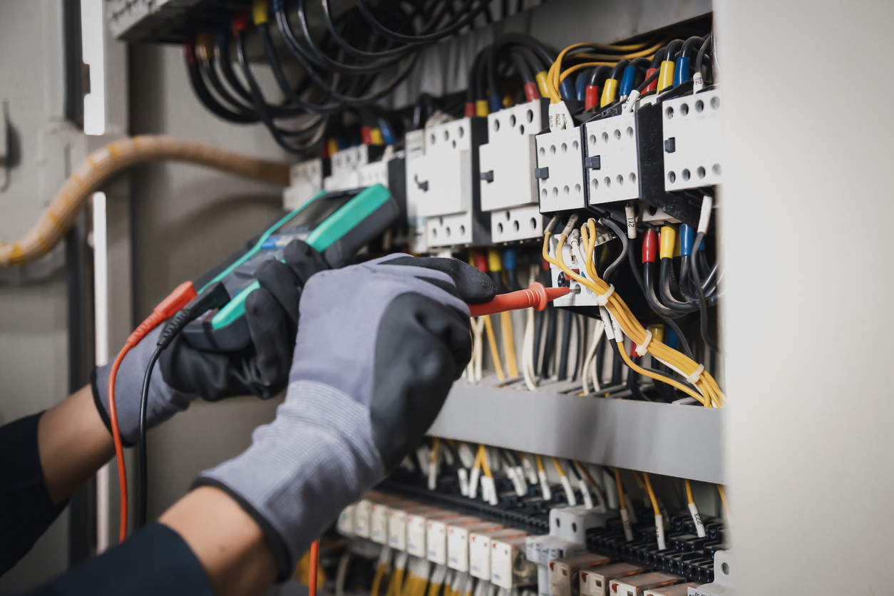 Engineer hand holding AC multimeter checking electric current voltage at circuit breaker terminal.